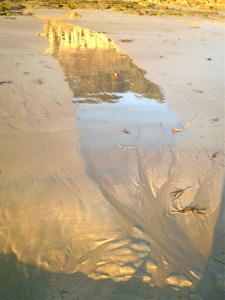 Sand and Reflection photograph with sunrise reflecting on rocks in turn reflected in wet sand.